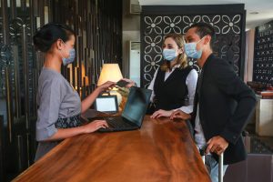 Couple,And,Receptionist,At,Counter,In,Hotel,Wearing,Medical,Masks
